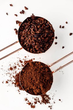 Beyaz arka planda kakao çubukları ve kakao tozu dolu gümüşten yapılmış altın ölçü bardaklar, bembeyaz gıda konsepti.