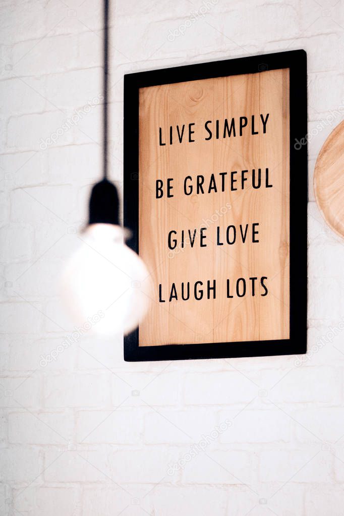 Inspiration quote frame hanging on the white bricks wall, Live simply Be grateful Give love Laugh Lots