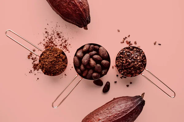 Rose altın bardak kakao çekirdekleri, kakao nips, kakao tozu ve pembe bir arka plan üzerine kakao bakla ölçme düz sağlıklı gıda kavramı yatıyordu