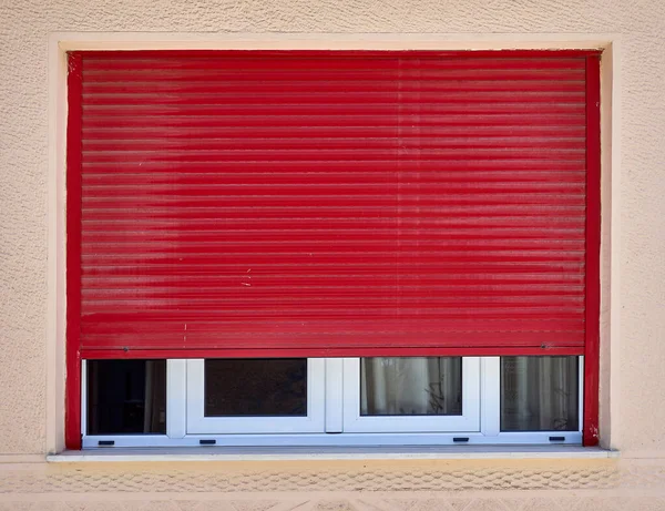 half open red rolling shutters window on light ocher wall