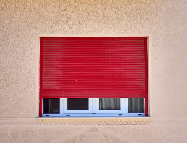 half open red rolling shutters window on light ocher wall