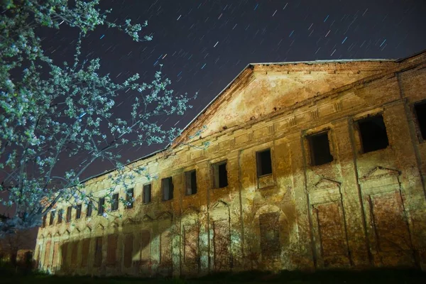 Right wing of count Potocki palace  in Tulchyn, Vinnytsia region, Ukraine, on a warm spring night against clear dark blue sky full of star tracks and youg apple tree in bloom