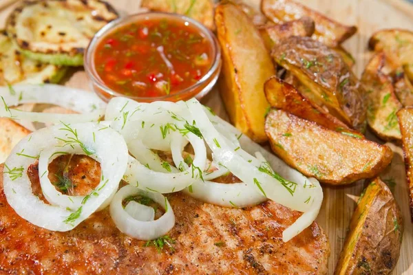 Grilled chicken meat with pickled onions and zucchini, french fries, served on wooden plate, closeup food photo