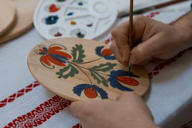 handpainting el yapımı dekoratif ahşap yuvarlak plaka üzerinde elini bir fırça, Petrykivka resim stili, son dokunuş parlak çiçek desenle boyar.