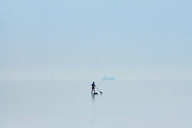 bir paddleboard onun elinde küreği ile üzerinde duran bir kadın figürü siluet, hala su yüzeyi, Gemi ufukta taşıma