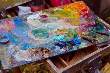 painter's wooden palette stained with a mess of fresh mixed colorful oil paints, rests on easel after artistic painting plainair, creative disorder clipart