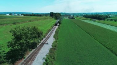 Tren geçerken Amish çiftlik arazileri ve kırsal yoluyla güneşli bir yaz günü dron tarafından görüldüğü gibi Buhar