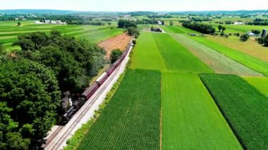 Tren geçerken Amish çiftlik arazileri ve kırsal yoluyla güneşli bir yaz günü dron tarafından görüldüğü gibi Buhar