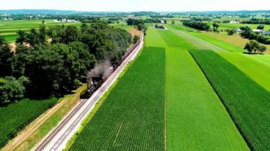 Tren geçerken Amish çiftlik arazileri ve kırsal yoluyla güneşli bir yaz günü dron tarafından görüldüğü gibi Buhar