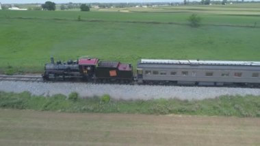 Ronks, Pennsylvania, Temmuz 2019 - Bir Drone tarafından görüldü olarak Güneşli bir Yaz Günü Amish Kırsal Boyunca Seyahat Yolcu Tren Puffing Duman ile 1910 Buhar Motoru Havadan Görünümü
