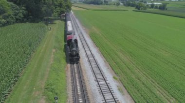 Ronks, Pennsylvania, Temmuz 2019 - Bir Drone tarafından görüldü olarak Güneşli bir Yaz Günü Amish Kırsal Boyunca Seyahat Yolcu Tren Puffing Duman ile 1910 Buhar Motoru Havadan Görünümü