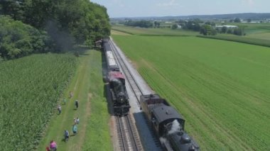 Ronks, Pennsylvania, Temmuz 2019 - Bir Drone tarafından görüldü olarak Güneşli bir Yaz Günü Amish Kırsal Boyunca Seyahat Yolcu Tren Puffing Duman ile 1910 Buhar Motoru Havadan Görünümü