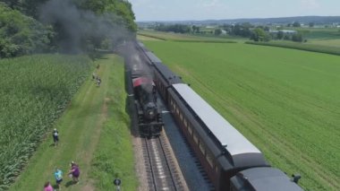 Ronks, Pennsylvania, Temmuz 2019 - Bir Drone tarafından görüldüğü gibi Bir Sunny Yaz Günü İkinci Bir Buharlı Tren Passes olarak İkinci Bir Buharlı Tren Olarak Amish Kırsal Boyunca Seyahat Yolcu Tren Puffing Duman ile 1910 Buhar Motoru Havadan Görünümü