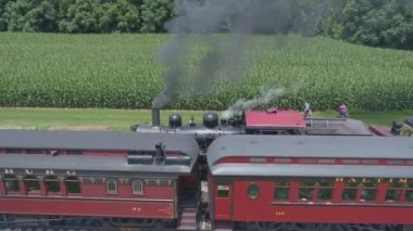 Ronks, Pennsylvania, Temmuz 2019 - Bir Drone tarafından görüldüğü gibi Bir Sunny Yaz Günü İkinci Bir Buharlı Tren Passes olarak İkinci Bir Buharlı Tren Olarak Amish Kırsal Boyunca Seyahat Yolcu Tren Puffing Duman ile 1910 Buhar Motoru Havadan Görünümü