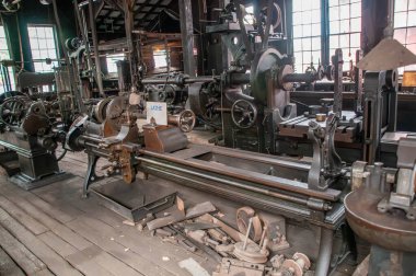 Bir torna da dahil olmak üzere çeşitli antika makinelerin sergilendiği tarihi bir atölyenin iç görünümü.