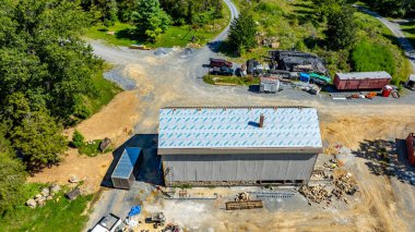 Yakında çakıl yolu olan kırsal bir alanda yeni bir bina bulunuyor. İnşaat malzemeleri ve yeşillik, doğa ve gelişimin bir karışımını sergileyerek sitenin çevresini sardı..