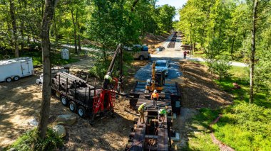 İşçiler ormanlık alanda bir patika inşa etmekle meşgul. Ağır makineler mevcut ve alan açık gökyüzü altında hareketlilik ile meşgul..