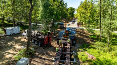 Elizabethtown, Pennsylvania, 8-26-2025 - İşçiler ağaçlık alanda inşaat araçları ve ekipmanları aktif olarak kullanımda olan bir patika inşa etmekle meşguller. Ayar yemyeşil ve yemyeşil.