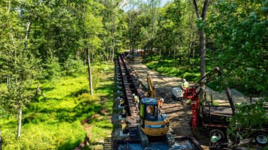 Elizabethtown, Pennsylvania, 8-26-2025 - Kazı makineleri ve kamyonlar da dahil olmak üzere ağır makineler verimli bir orman ortamında aktif olarak bir inşaat projesiyle meşgul. İşçiler görünür.