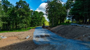 İşçiler doğal ortamdaki ağaçlarla çevrili bir çakıl yolu inşa ediyorlar. Gökyüzü birkaç bulutla açık. Açık havada çalışmak için güzel bir hava var..