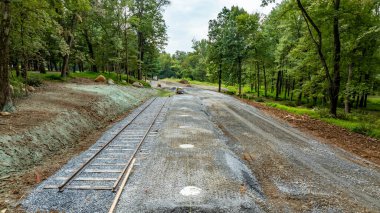 Orman bölgesinde yeni döşenmiş demiryollarının yanına çakıllı bir yol inşa ediliyor. Çevreleyen ağaçlar gölge sağlar ve manzara gelişimin ilk aşamalarındadır..
