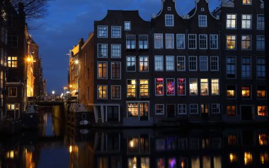 Amsterdam, Hollanda geceleri bir kanal üzerinde tarihi evlerin ışıklı windows