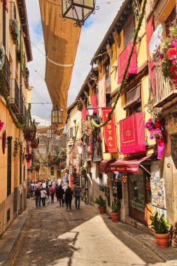 Toledo, İspanya - 28 Mayıs 2016: İspanya 'nın tarihi Toledo kentinde düzenlenen Corpus Christi festivali sırasında çiçeklerle süslenmiş bir sokakta yürüyen turistler