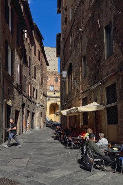 Siena, İtalya - 29 Eylül 2017: Turistler 29 Eylül 2017 tarihinde İtalya 'nın Siena kentinde büyük malikaneleri olan dar bir sokakta kaldırım restoranında garson tepsisi taşıyarak oturuyorlar.
