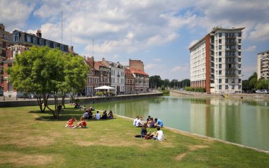 Lille, Fransa - 1 Haziran 2017: İnsanlar 1 Haziran 2017 'de Fransa' nın Lille kentindeki Quai du Wault parkının sularında tarihi ve modern yerleşim binalarında çimlerin üzerinde otururlar..