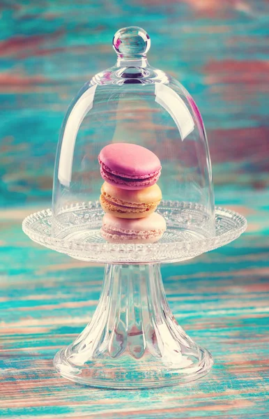 Macaroons in glass bell jar on wooden table