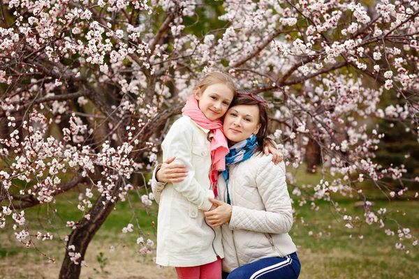 Giovane donna felice con la sua bambina. Madre che cammina con la figlia in un giorno di primavera. Genitore e bambino godendo stagione dei fiori di ciliegio. Bambino che indossa concetto — Foto Stock