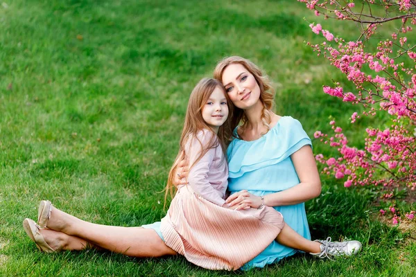 Junge schöne Frau mit einer kleinen Tochter, die durch die blühende sakura.the Konzept der Familie Ruhe und Liebe. — Stockfoto