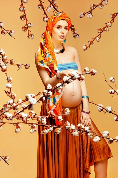 Uroda Kobieta w ciąży z bawełny kwiaty stwarzające przeciwko żółtym tle w Studio — Zdjęcie stockowe