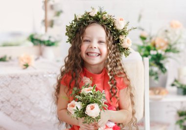 Çocuk- çiçek tacındaki kız. Parlak bir stüdyoda Güzel küçük kız oturur, lauht ve kameraya bakar