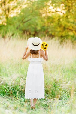 Sarı bir alanda gün batımında ayakta beyaz bir elbise güzel bir hamile kız tam uzunlukta fotoğraf. Geri görünüm.