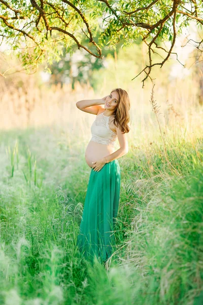 Słodka, uczciwa dziewczyna w ciąży w zielonej spódnicy stoi w parku. — Zdjęcie stockowe