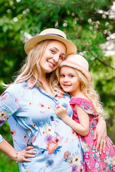 Madre embarazada con su hija abrazándose en el parque en un día soleado de verano . —  Fotos de Stock