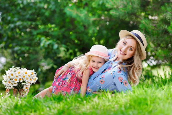 Portraitof a beautiful pregnant mother in a straw hat lie near to her little daughter in a park on a sunny summer day. The concept of happy family relationships. — Stock Photo, Image
