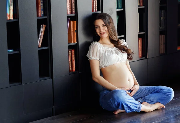 Heureuse femme enceinte asiatique en t-shirt blanc et jean bleu tenant le ventre avec les mains et riant isolé sur fond noir — Photo