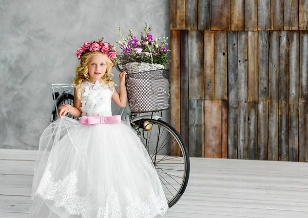 Cute Little Girl w pięknej bujnej białej sukni w Wieniec kwiatów na głowie stoi w studiu obok roweru — Zdjęcie stockowe