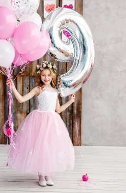 Taze çiçekler ve zarif pembe elbise bir çelenk güzel bir küçük kız beyaz bir stüdyoda onu dokuz doğum günü kutluyor.