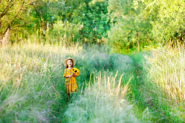 Bambina con un bouquet di fiori gialli selvatici in piedi nel prato soleggiato giorno d'estate in un cappello di paglia. Copia spazio — Foto Stock