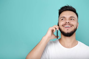 Yakışıklı genç beyaz t-shirt telefon kullanarak ve parlak konuşurken gülümseme hipster sakallı. Kopya alanı.