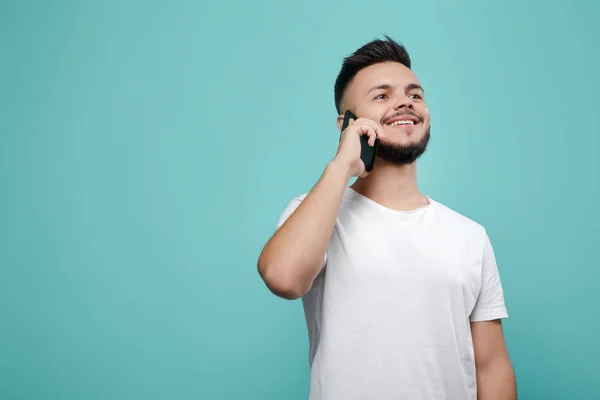 Młody przystojny Brodaty hipster w biały t-shirt, przy użyciu telefonu i rozmawia z jasny uśmiech. Miejsce. — Zdjęcie stockowe