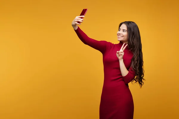 Attractive young lady taking selfie posing in studio in front of orange background. — Stock Photo, Image