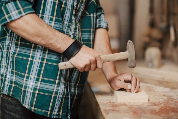 Tischler nagelt Holzbretter mit Hammer auf Holztisch in der Werkstatt. — Stockfoto