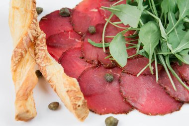 Siyah ahşap zemin üzerine bir tabakta lezzetli kurutulmuş sığır eti basturma peynir, mozzarella peyniri, patates ve ıspanak yaprakları.