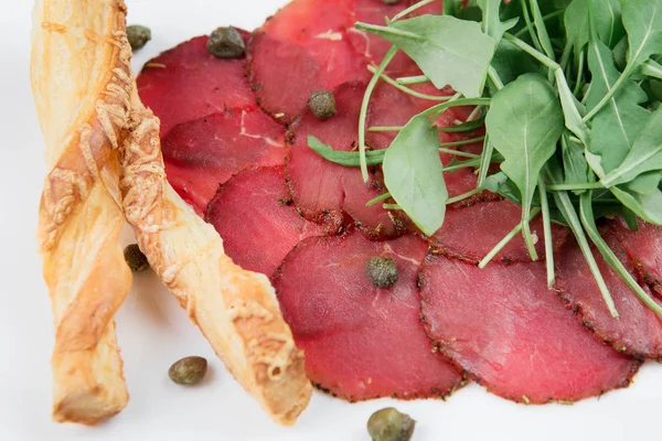 Siyah ahşap zemin üzerine bir tabakta lezzetli kurutulmuş sığır eti basturma peynir, mozzarella peyniri, patates ve ıspanak yaprakları.