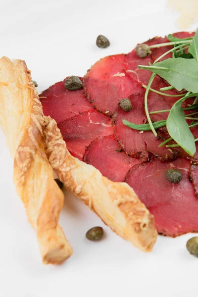 Siyah ahşap zemin üzerine bir tabakta lezzetli kurutulmuş sığır eti basturma peynir, mozzarella peyniri, patates ve ıspanak yaprakları.