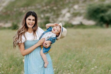 Littlte bebek oğlu ile alan çiçekli dağ yoluyla oynamaya uzun mavi bir elbise içinde mutlu genç anne.